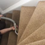 Person using a professional cleaning tool to clean a beige carpeted staircase