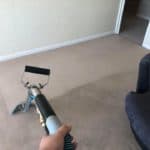 Person holding a carpet cleaning tool over beige carpet showing a clean area in front of a sofa