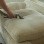 Person cleaning a beige sofa with a professional upholstery cleaning machine